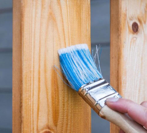 post-two Professional painter applying a fresh coat of protective paint to a wooden garden fence with a brush.